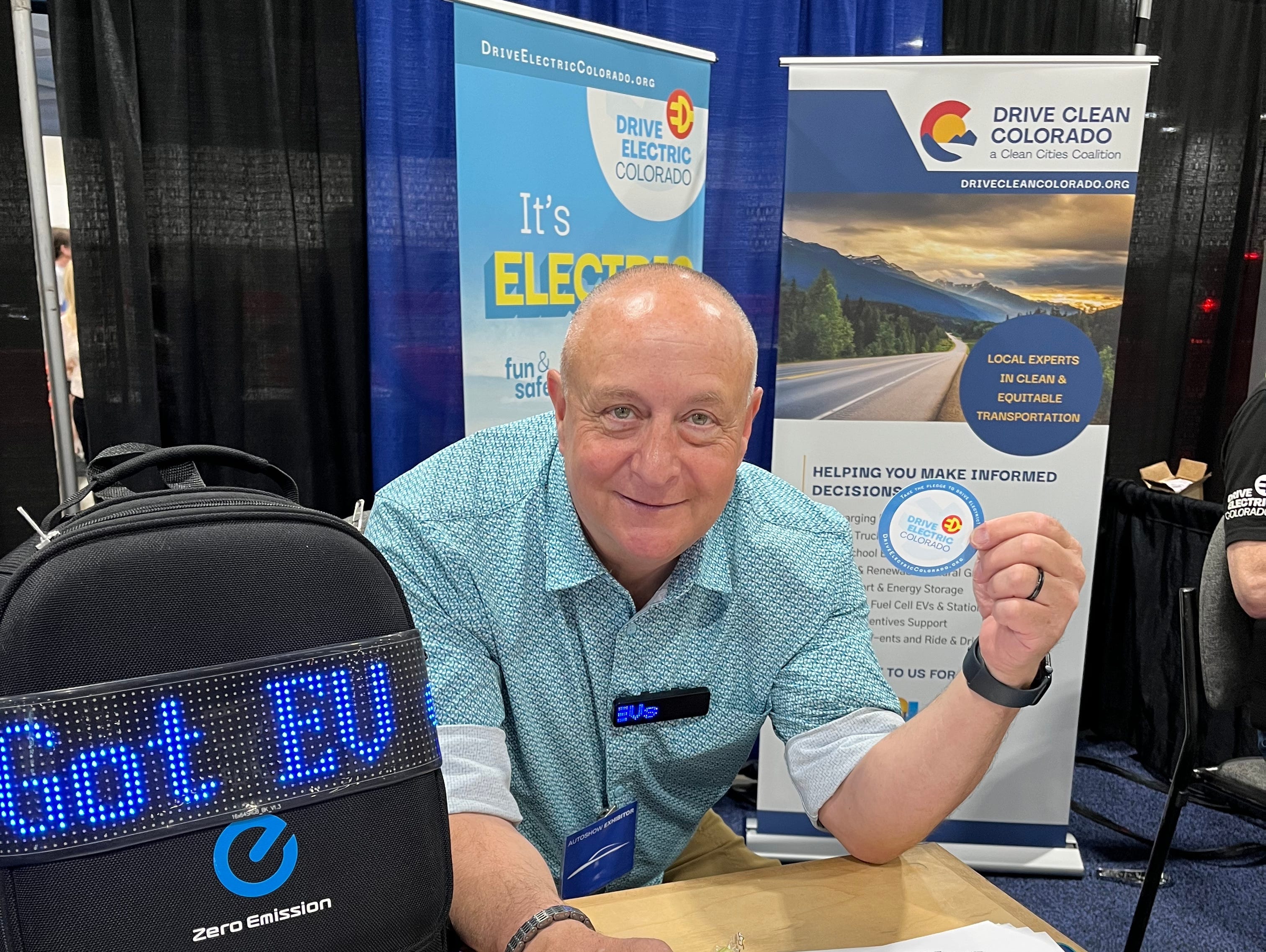 A man stands in front of an EV booth at an industry expo.