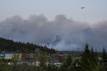 A helicopter carrying water flies over heavy smoke from an out-of-control fire in a suburban community outside of Halifax that spread quickly, engulfing multiple homes and forcing the evacuation of local residents on Sunday May 28,