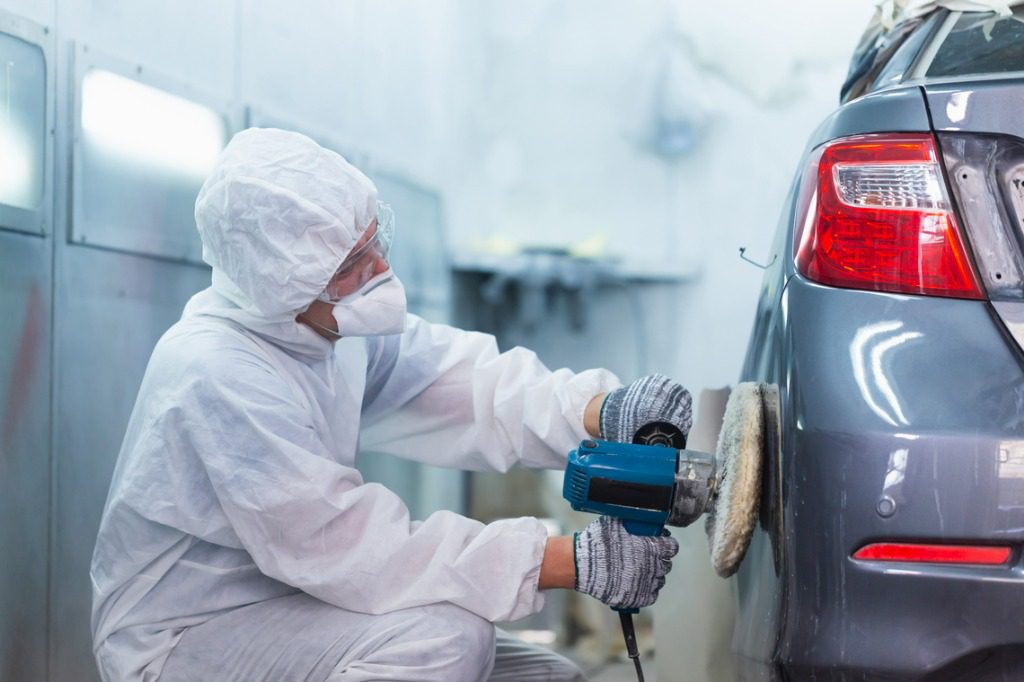 Car repair person buffing out paint after replacing body parts.