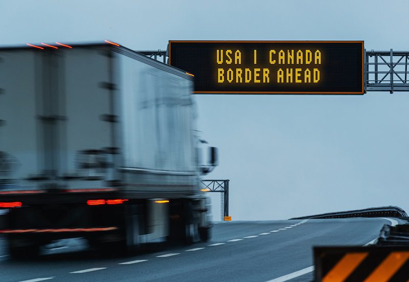 Semi truck approaching a border ahead highway sign.
