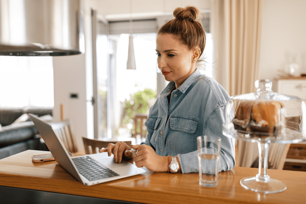 Caucasian woman sitting in her kitchen, studying online on her laptop.