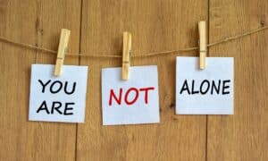 three clothespins on a string, each holding a piece of cheesecloth that say "you are," "not," and "alone"