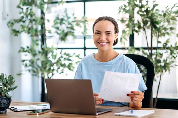 Woman sitting at her desk with her laptop, holding a printed quote for a million dollar whole life insurance policy.