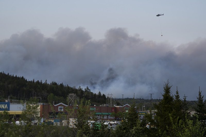 A helicopter carrying water flies over heavy smoke from an out-of-control fire in a suburban community outside of Halifax.