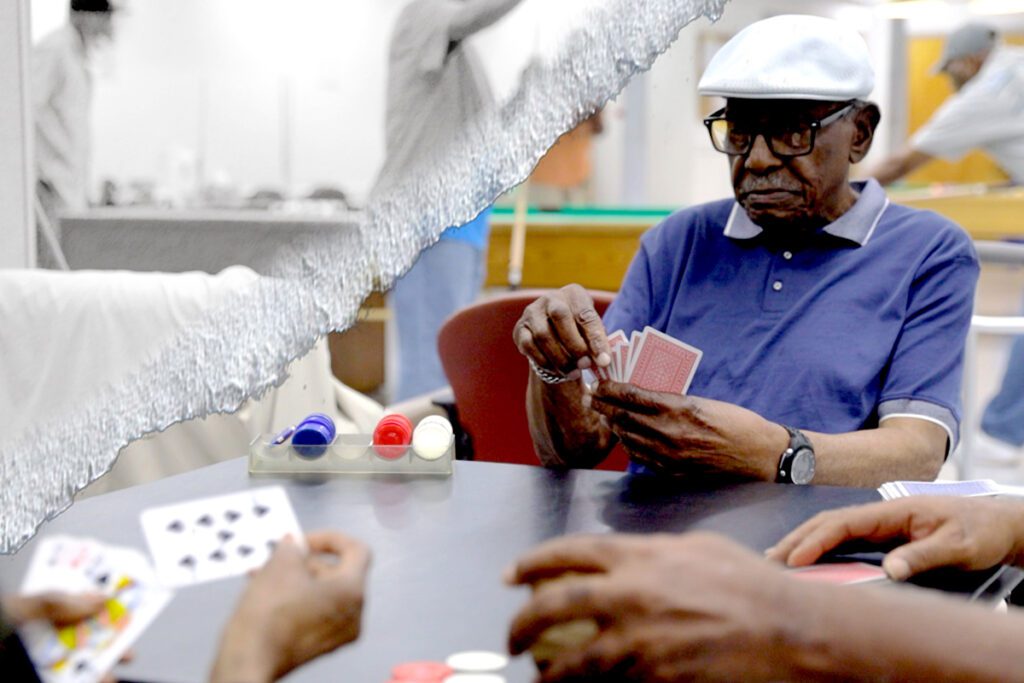 A mature man plays a card game with others in a senior center.