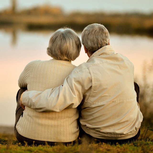 An older couple sitting by a calm lake.