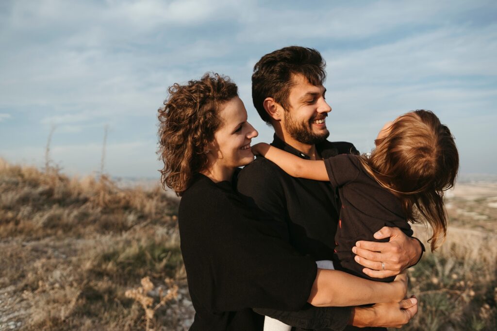 Young happy family holding their little daughter and hugging outdoors. Happy family activity together