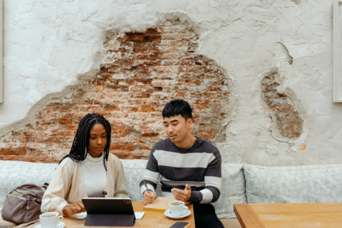 Friends sitting by modern coffee shop table discussing project on tablet device while having coffee