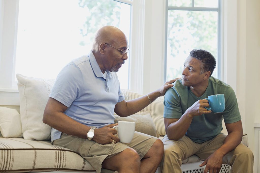 Senior father and son talking while having coffee on sofa