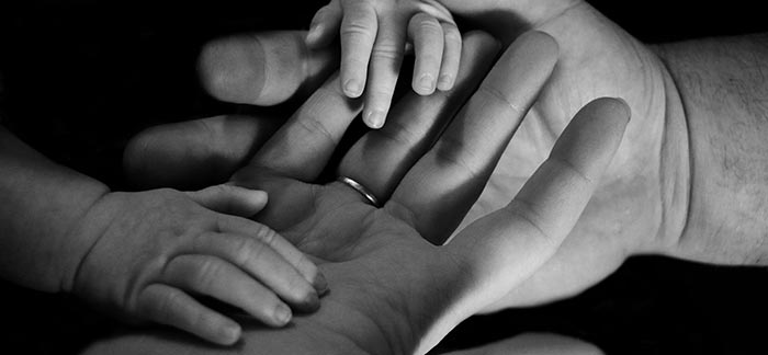 Image of baby's hands in mom and dad's hands for Quotacy blog What Is a Trust?