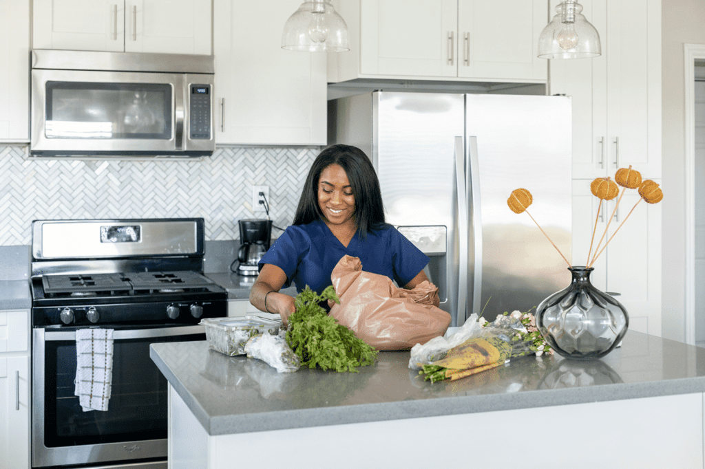 Woman unpacks healthy groceries and flowers.