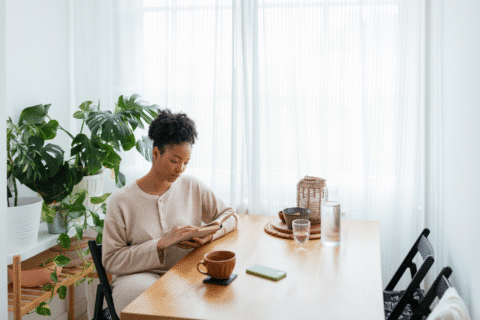 Woman sitting at the table in the kitchen at home, reading a book.