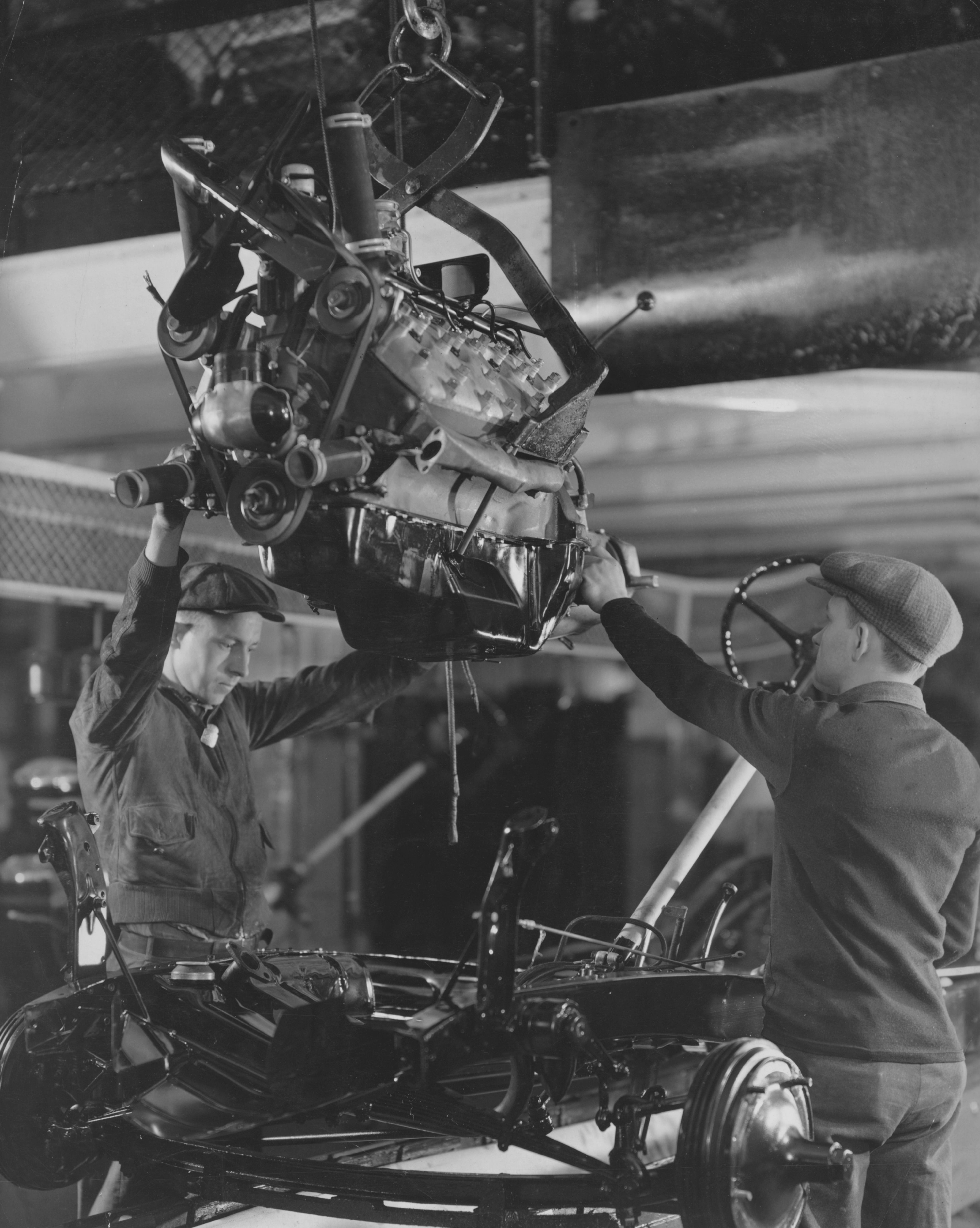 Factory workers assembling an engine in the body of a car, USA, circa 1930.