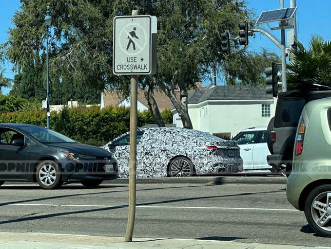 Rear 3/4 view of a camouflaged next-gen Audi S5 Sportback in traffic from far away