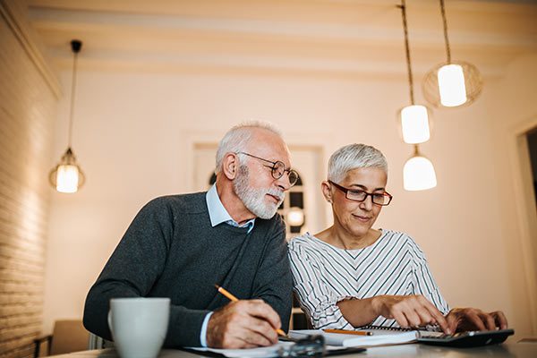 Senior couple with a notebook and calculator making a financial plan that includes cash value life insurance