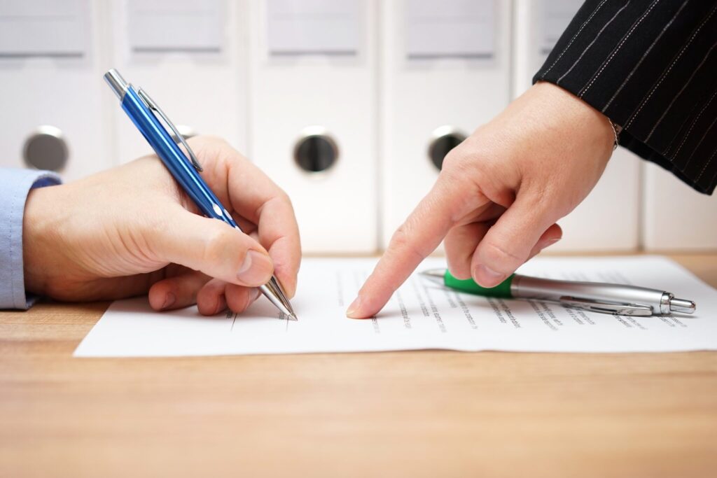 business woman is pointing where to sign on document, with documents in background