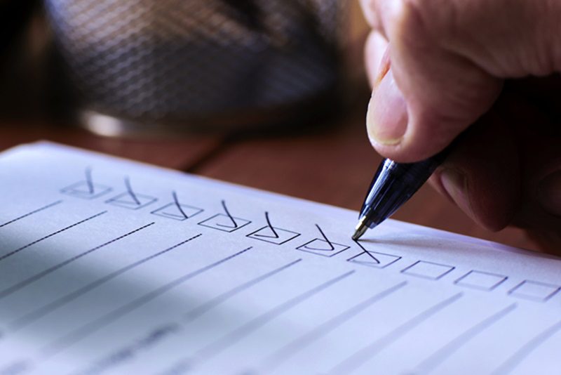 Close up image of a person’s hand using a ballpoint pen to put a check or tick mark in a row of boxes on a paper form sheet.