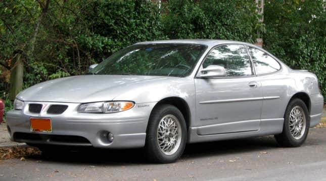 A silver Pontiac Grand Prix Coupe parked in front of some greenery