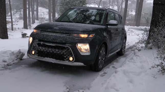 A Kia Soul driving through a snowy wooded area covered in ice.