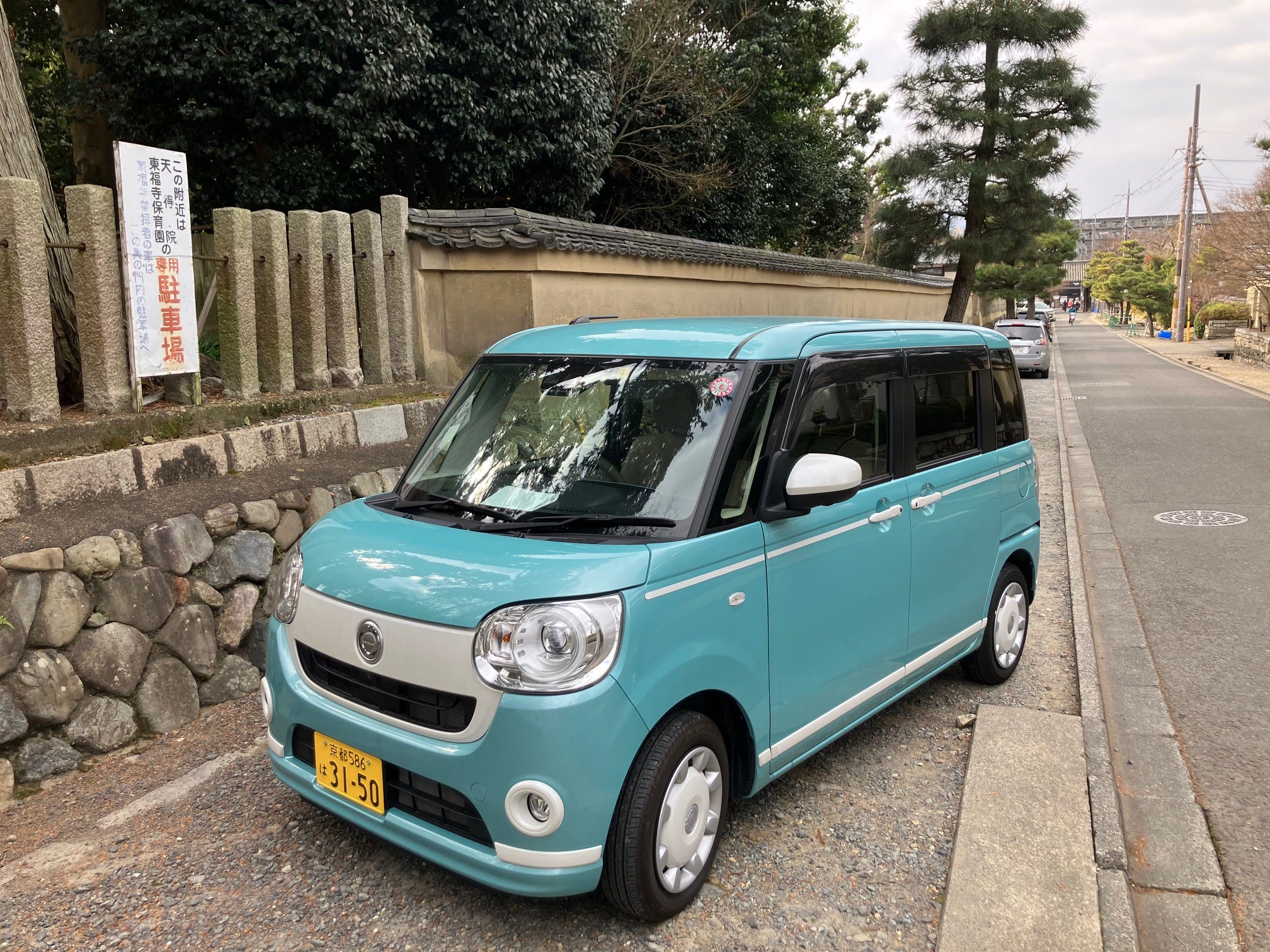 A Diahatsu Canbus "kei" car is parked on the side of a road in Kyoto, Japan