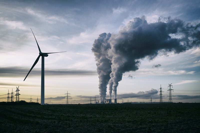 Single wind turbine, a coal burning power plant with pollution and electricity pylons in the background.