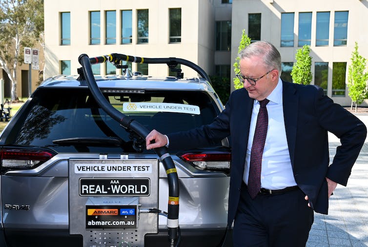 man in suit stands next to electric vehicle