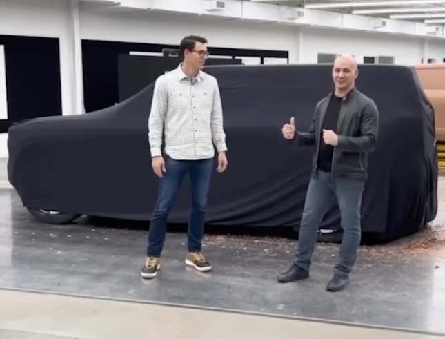 Two men standing in front of a covered Rivian R2 clay model