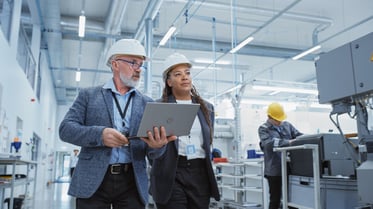 Image of two people walking in a factory with a laptop.