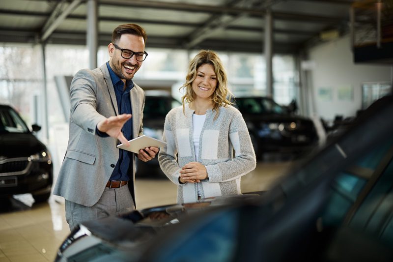 Happy salesman selling the car to his female customer in a showroom.