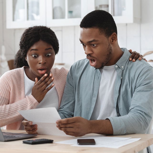 A couple sitting at a table looking at papers in shock