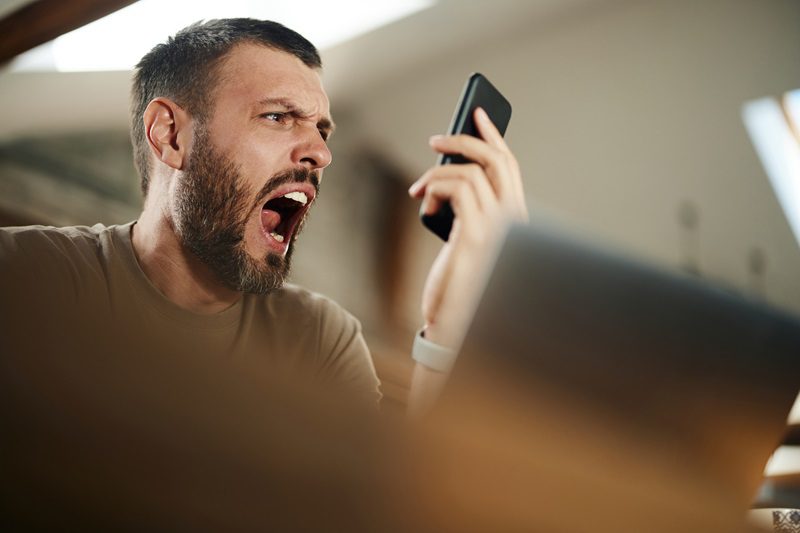 Frustrated man screaming on someone through a call over smart phone at home.