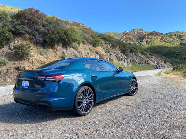 A rear 3/4 shot of the car parked in front of grassy rocky hills