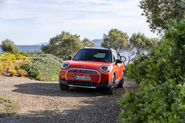 An orange Aceman SE driving on a gravel road near plants