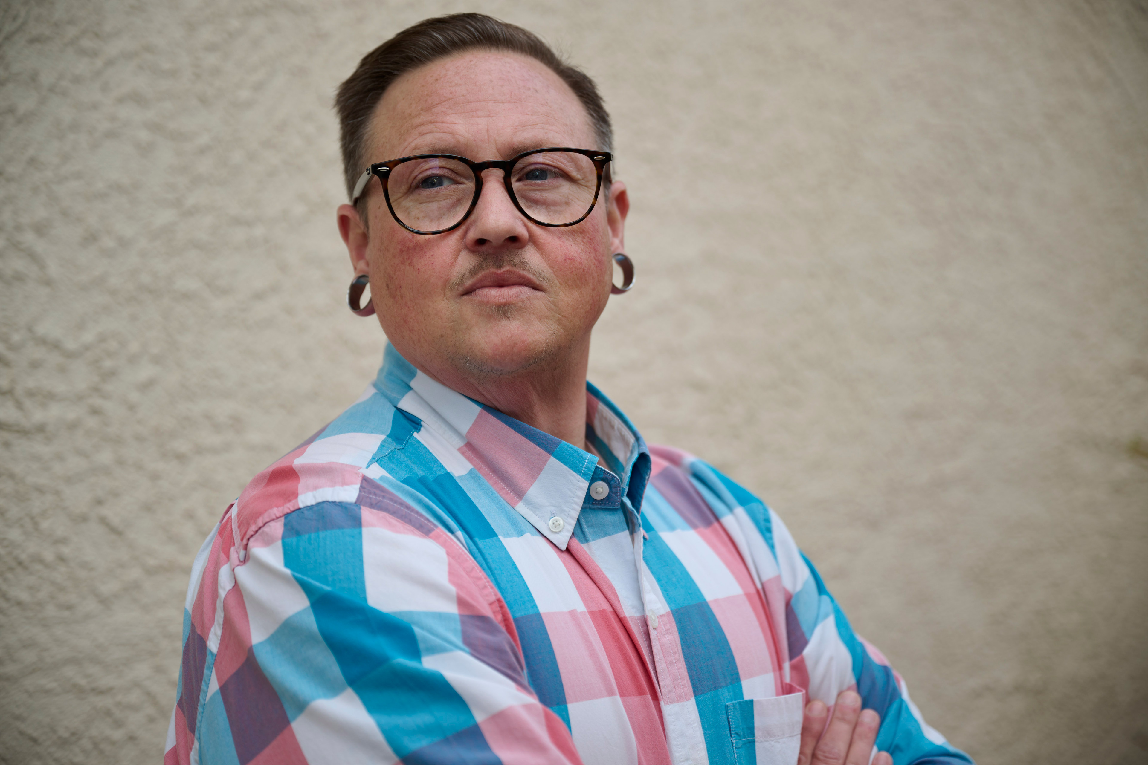 A photo of a man standing outside with his arms crossed. He's looking away from the camera.