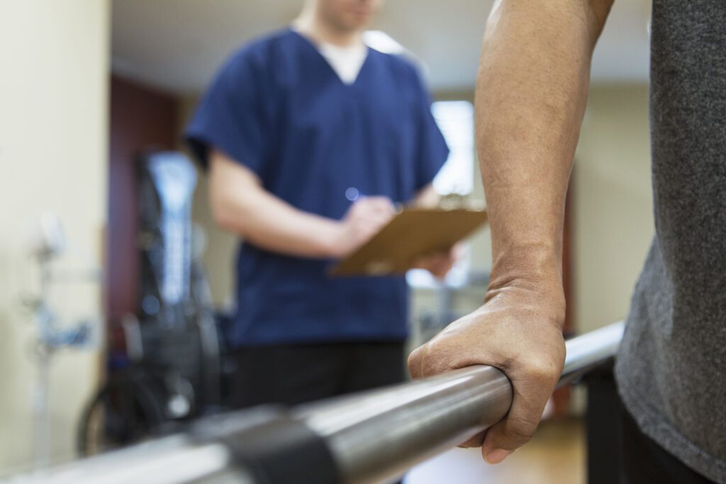 An unidentifiable patient is undergoing physical therapy while a health care professional takes notes behind them.