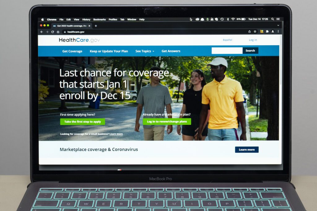 A photograph of a laptop. On the screen is the homepage for healthcare.gov.