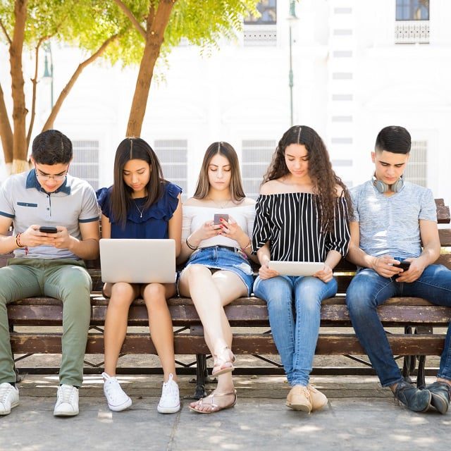 Group of teenagers social networking using several tech devices;