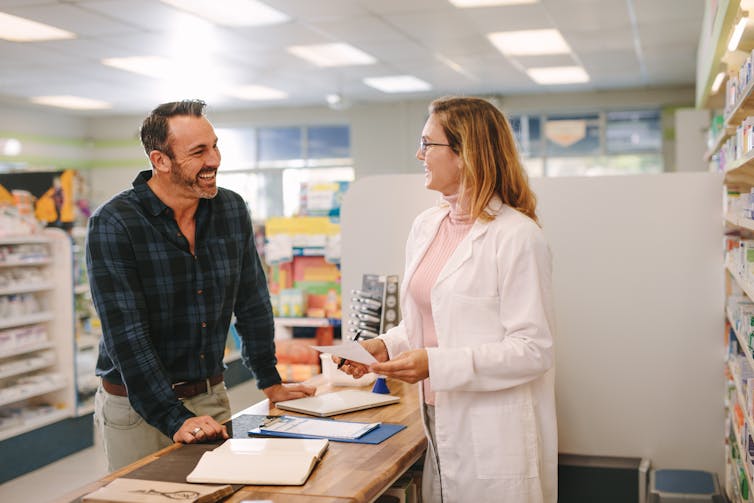 A male customer talking to a female pharmacist. Both are smiling.