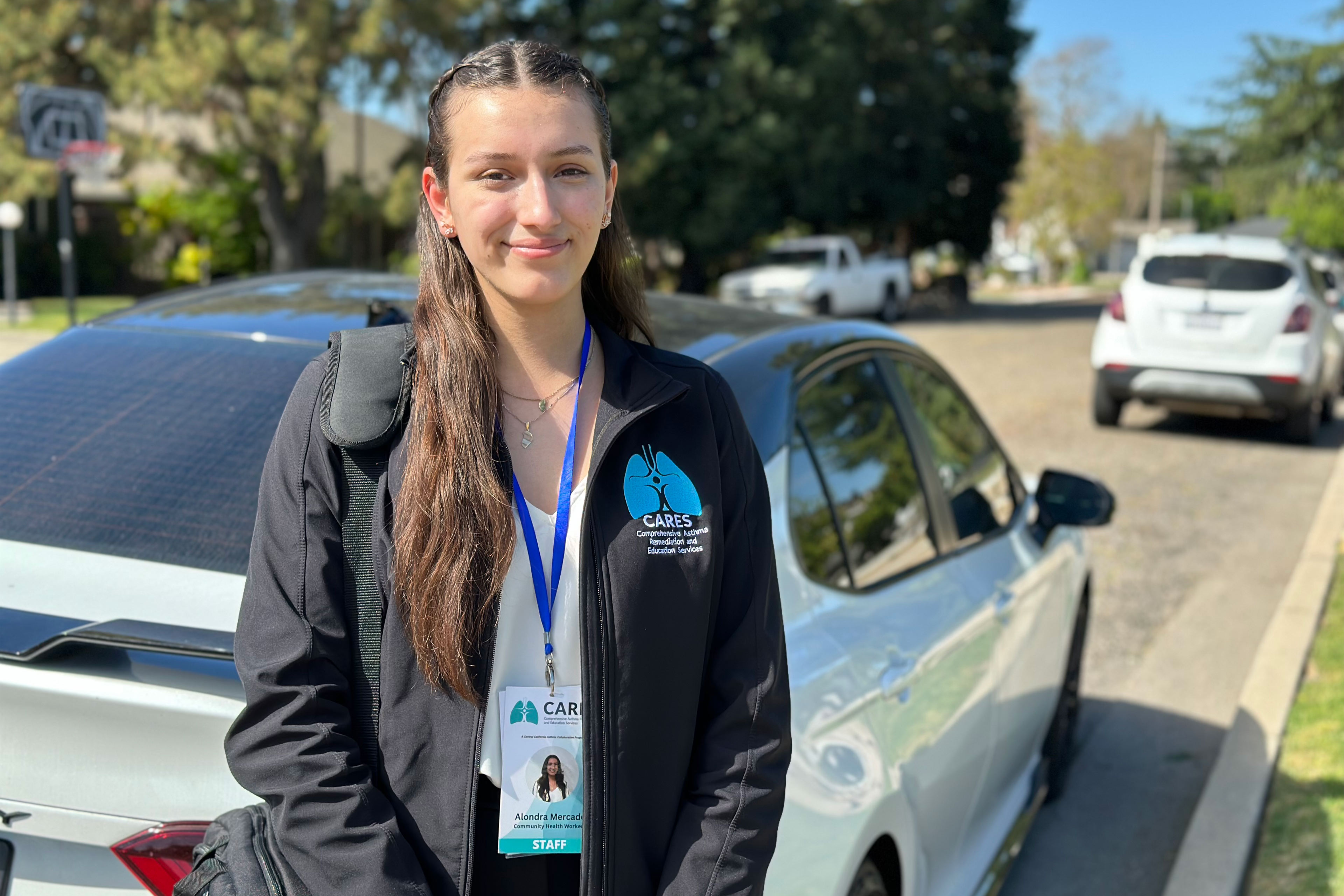 A photo of a community health worker posing for a portrait outside in front of a car.