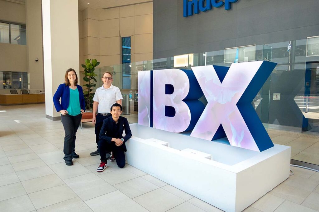 Marie Thresher, Chris Counter, and Calvin Tan alongside the IBX letters displaying the projection mapping