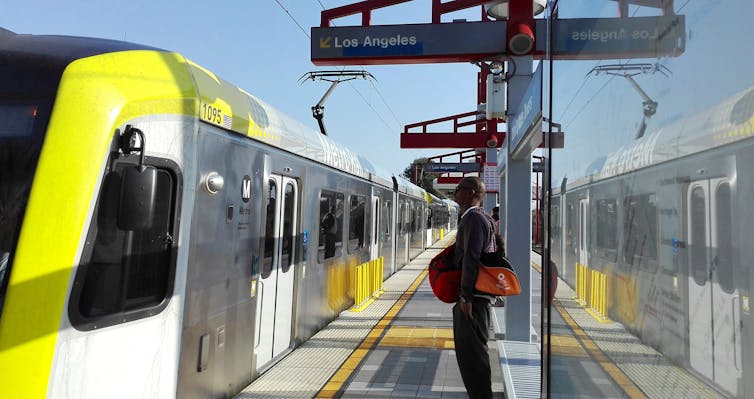 Main waits for arriving train on platform beneath sign that says Los Angeles