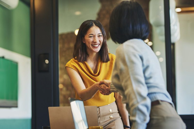 Businesswoman shaking hands with client and smiling cheerfully in meeting room