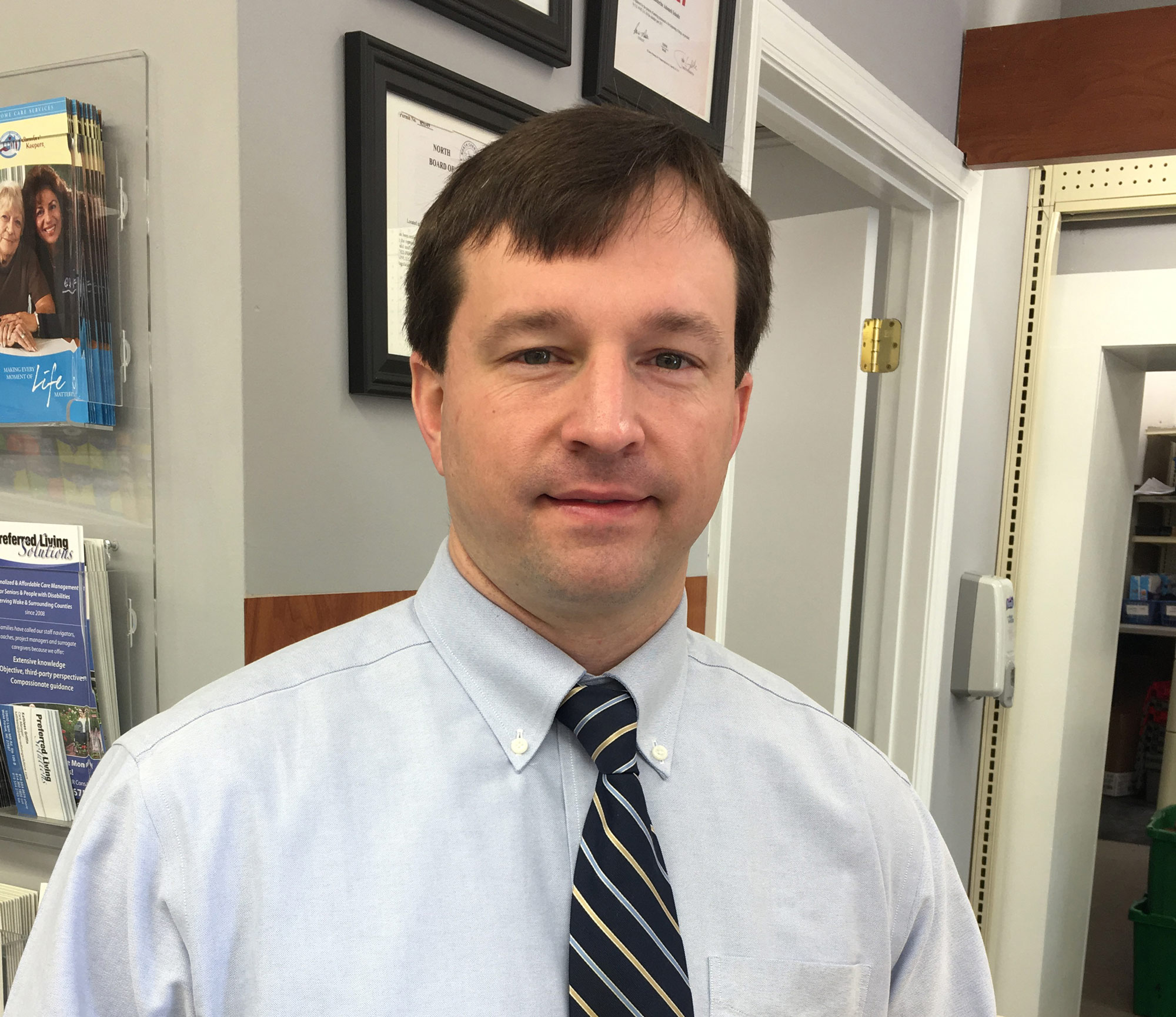 A photo of a man in a button-up shirt and tie smiling for a photo indoors.