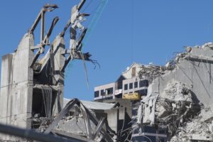 "Christchurch, New Zealand - April 28, 2012: Framed by the rubble from the former Crowne Plaza Hotel demolition, the earthquake damaged Price Waterhouse Coopers building is being prepared for demolition by Nikau Contractors Limited."