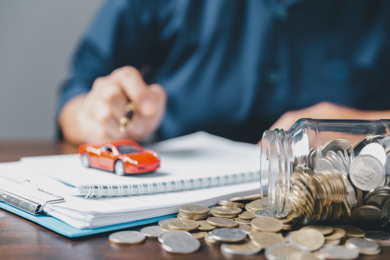 Toy auto mobile on top of a stack of note books and beside a spilled jar of coins