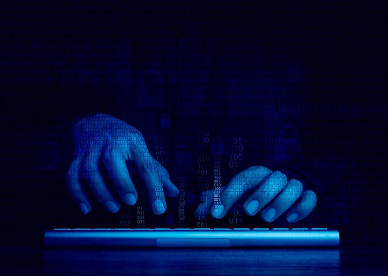 Hackers' hands typing on keyboard on a dark blue background.