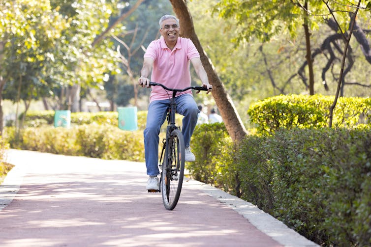 A smiling older man ride a bicycle along a cycle path through a park