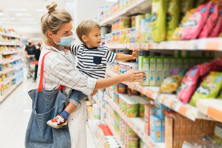 A woman holding a young boy while looking at products on a supermarket shelf.