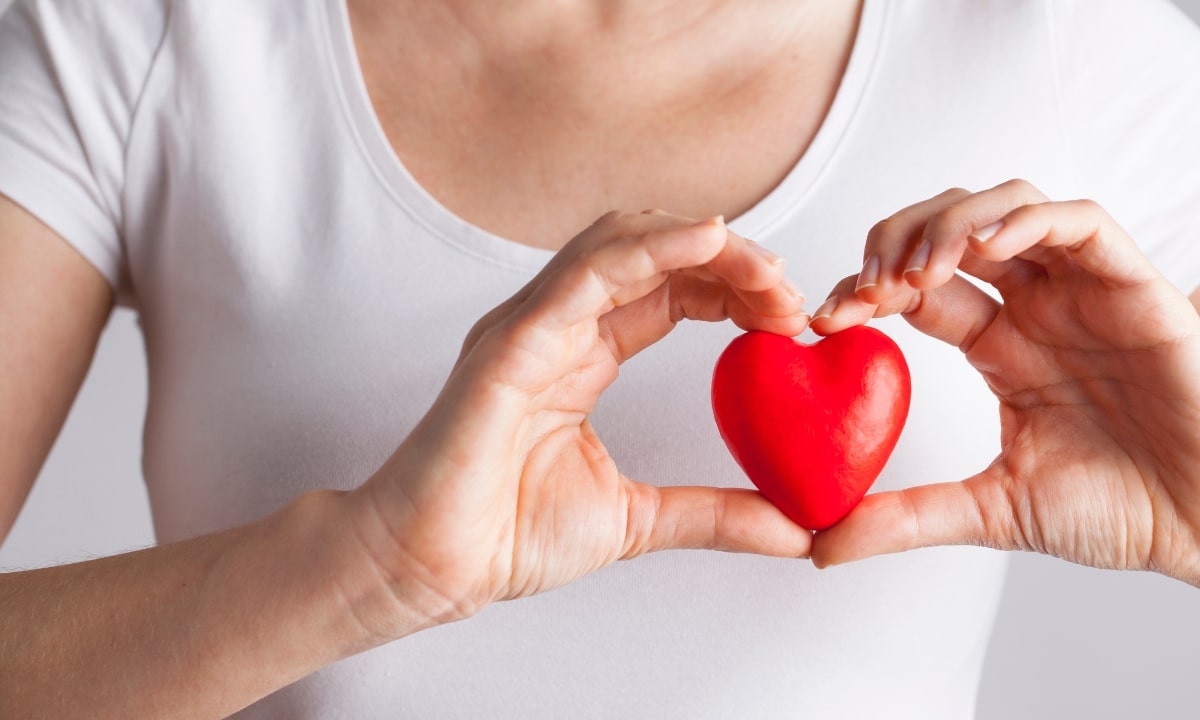 a woman in a white shirt holding a red heart above her own