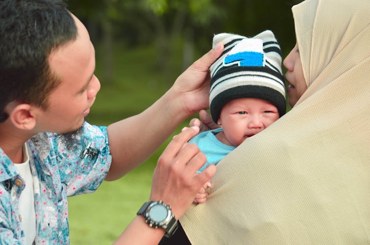 A man strokes a baby held by a woman in a hijab.